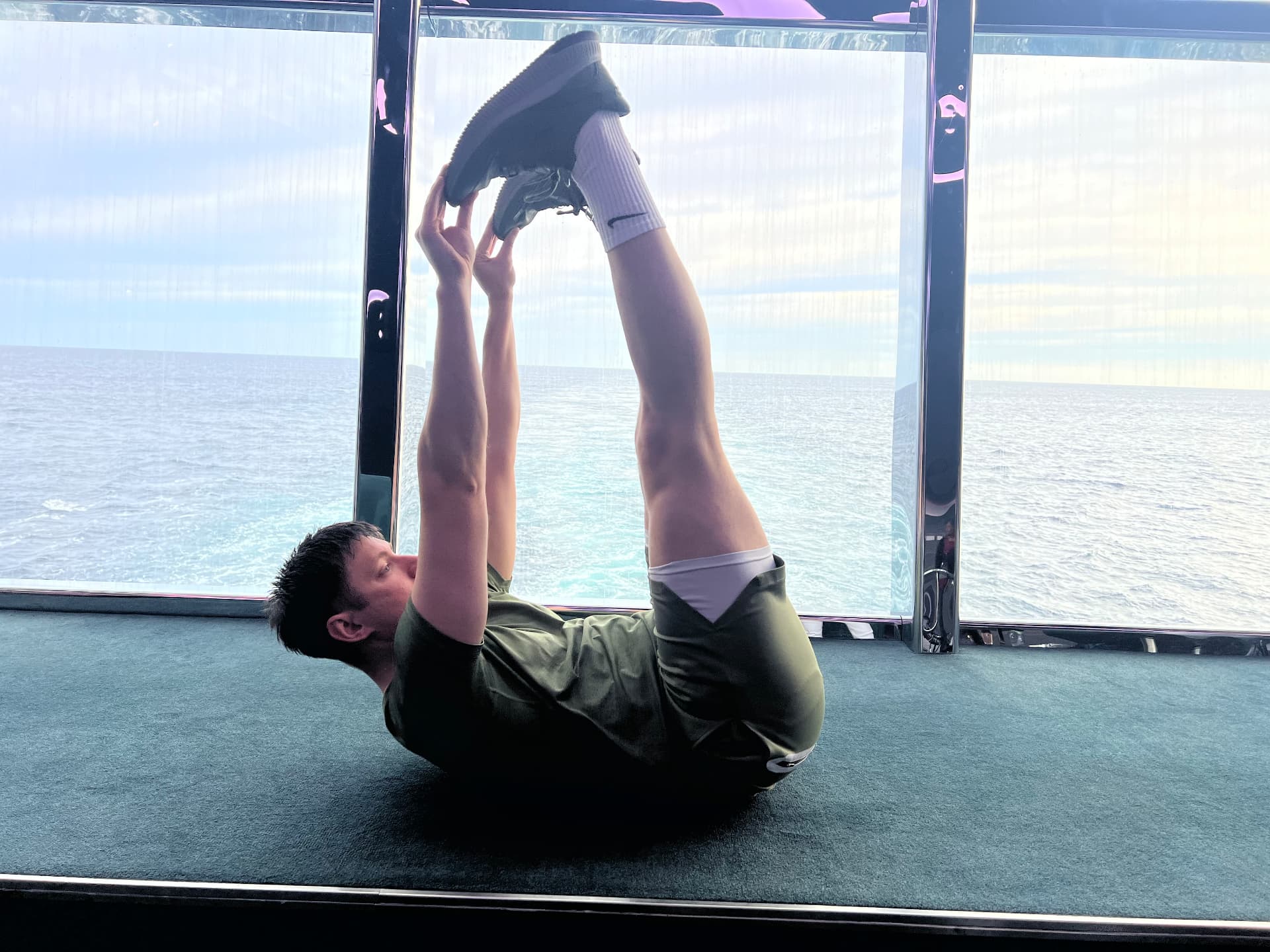 Jason drawing both legs overhead in a Pilates roll-over by the sea