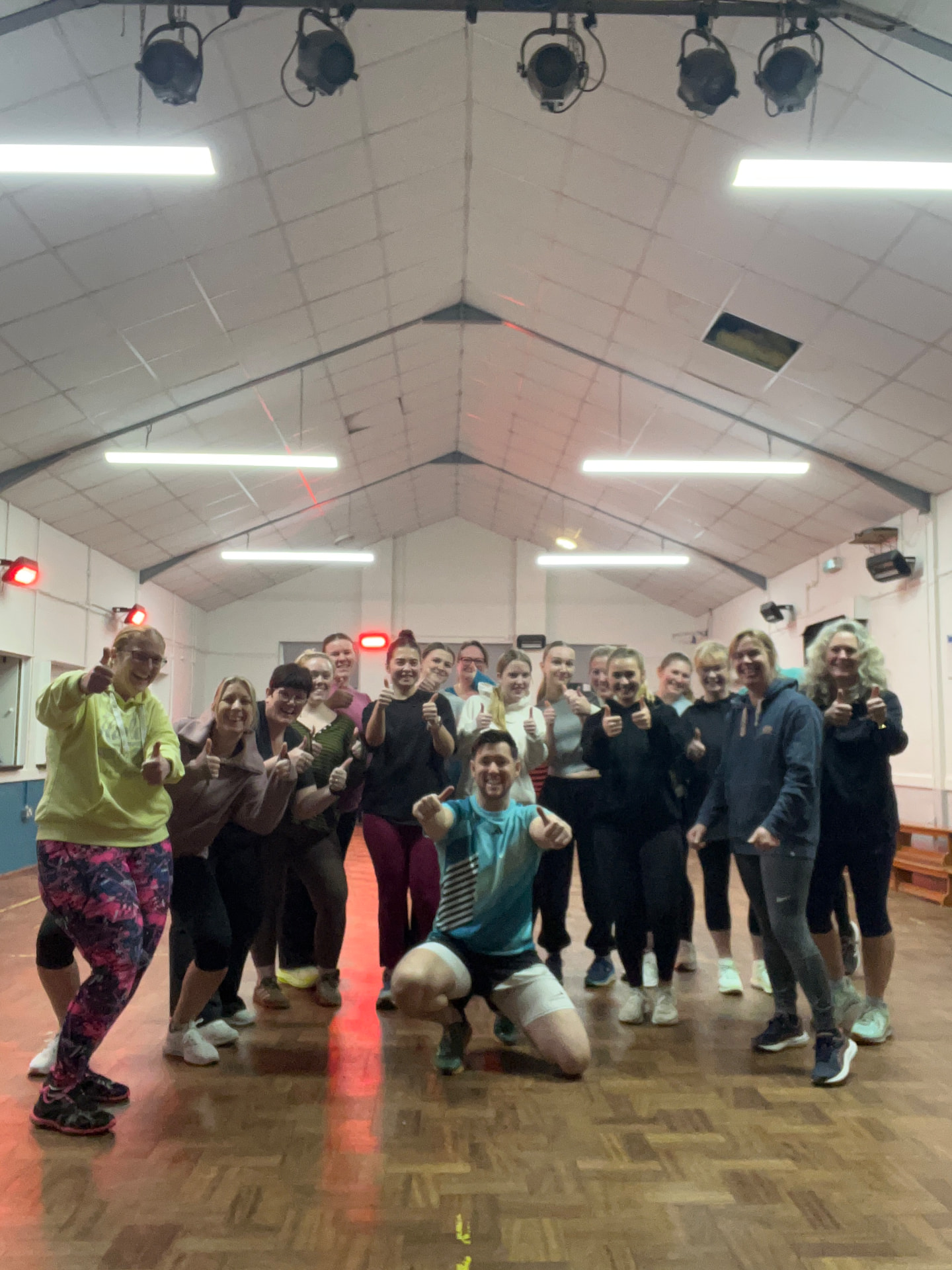 Jason kneeling with his class giving thumbs up in a village hall