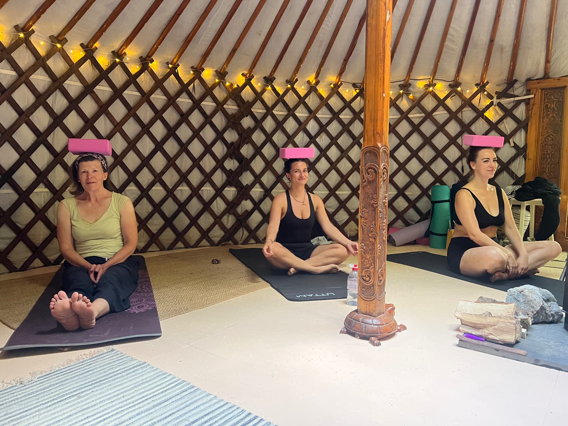Three retreat guests seated on mats in the yurt balancing pink blocks on their heads