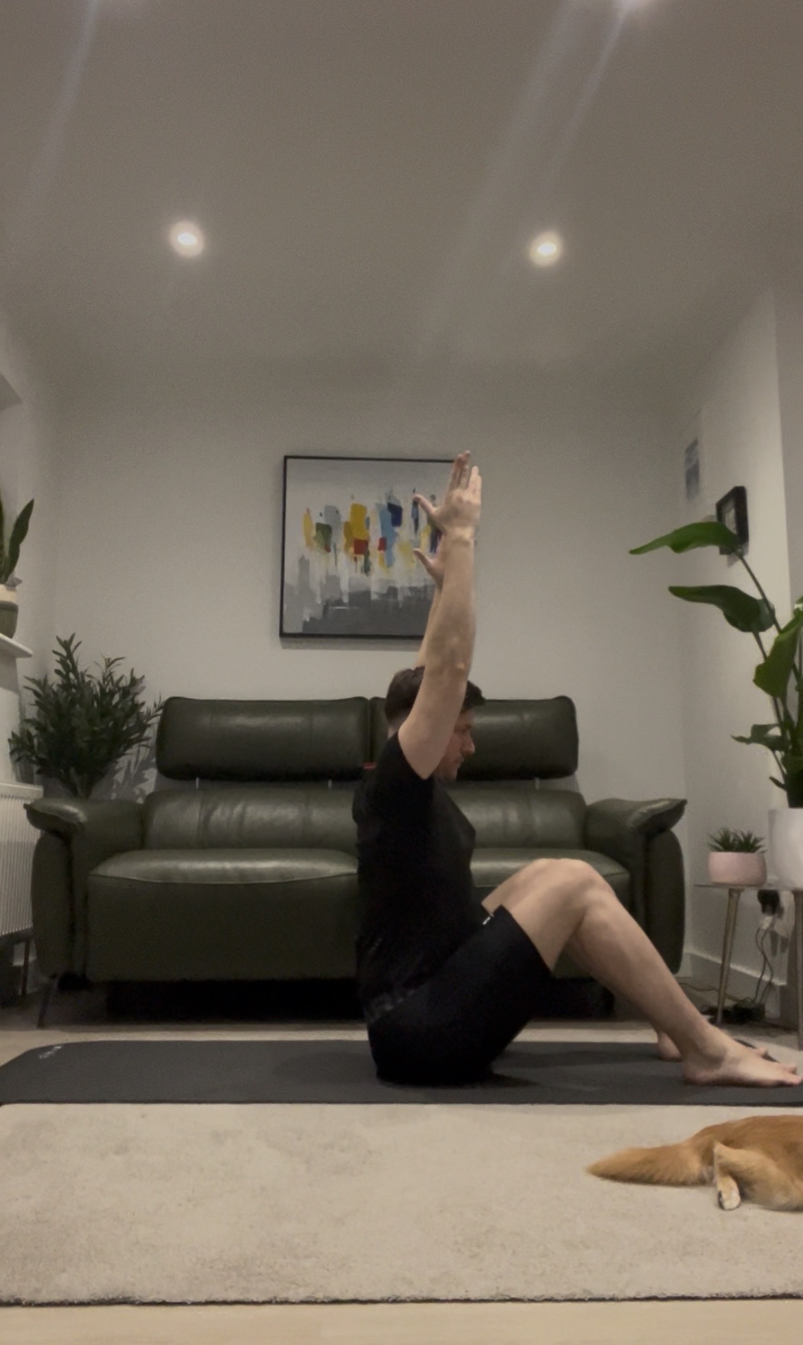 Jason demonstrating a seated Pilates roll-up with arms reaching overhead