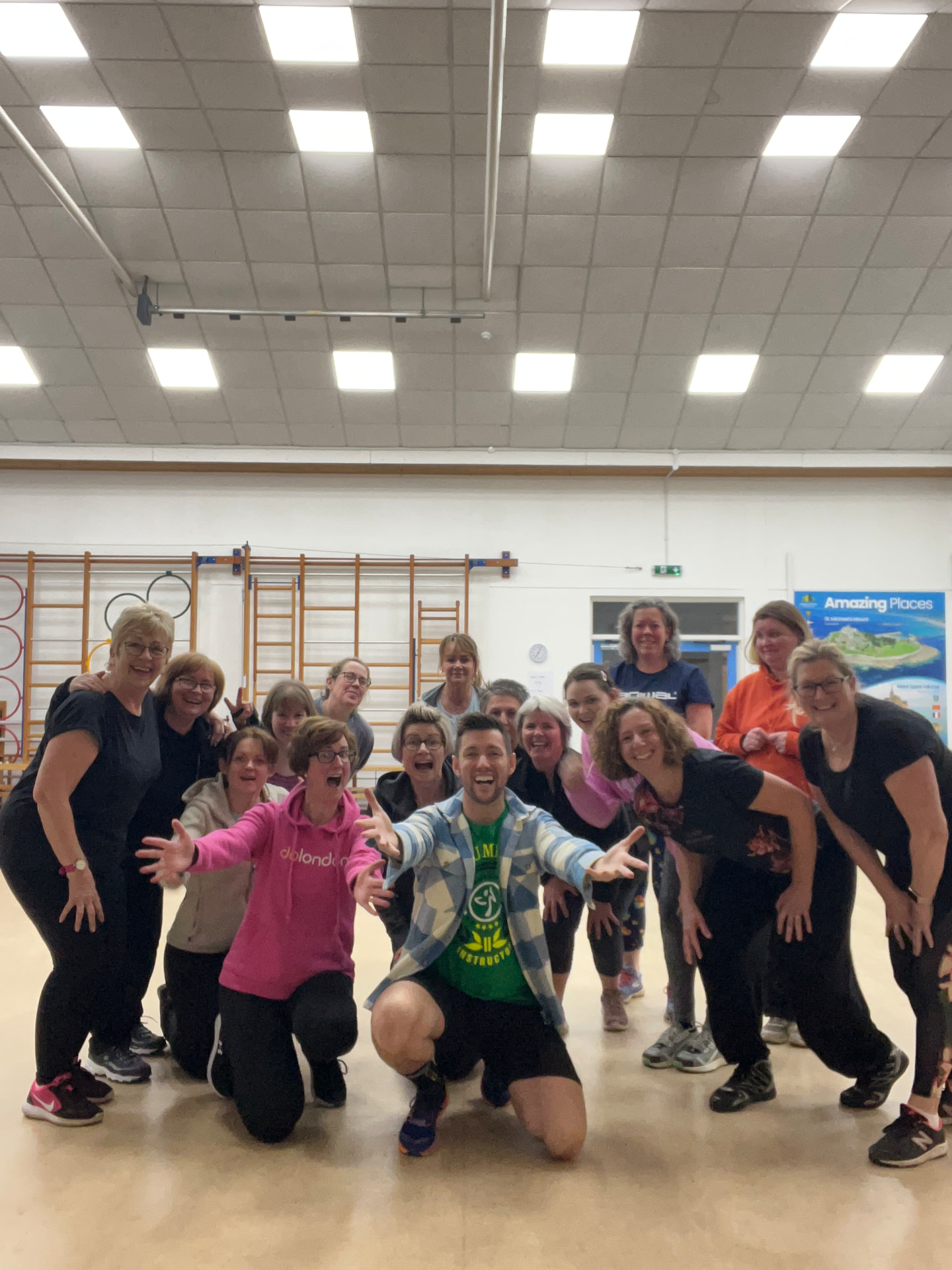 Jason kneeling with arms outstretched surrounded by his laughing Zumba class