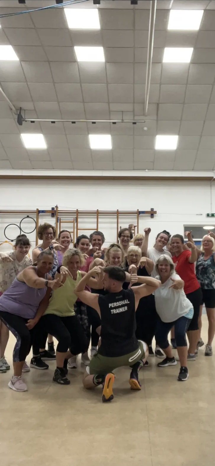 Jason kneeling with his class flexing and posing after a fitness class