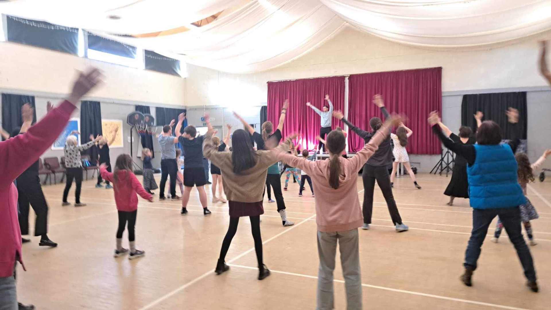 Community dance class following Jason from the stage in a village hall